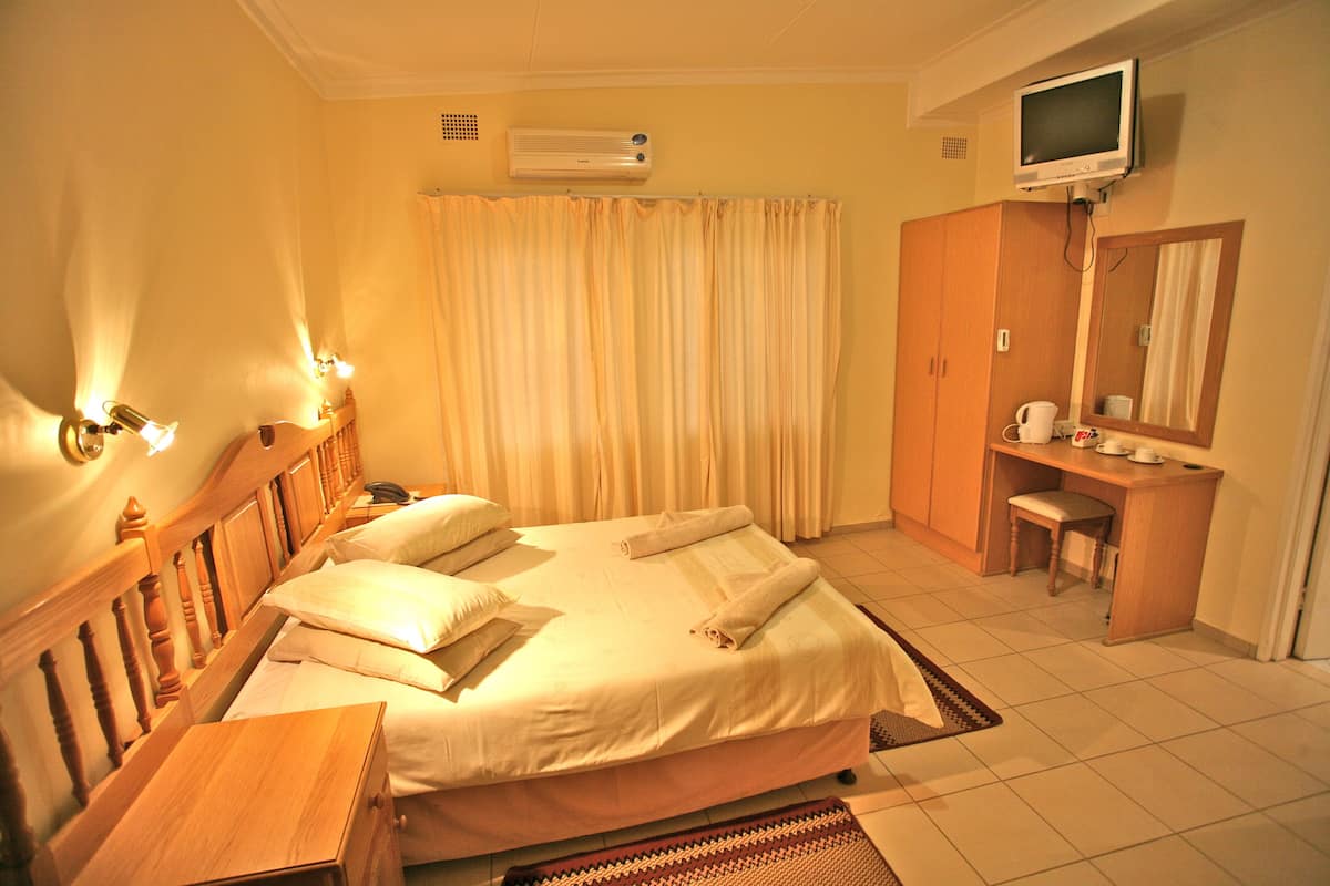 A hotel room with a bed, bedside table, a desk with a chair, a television, and a mirror.