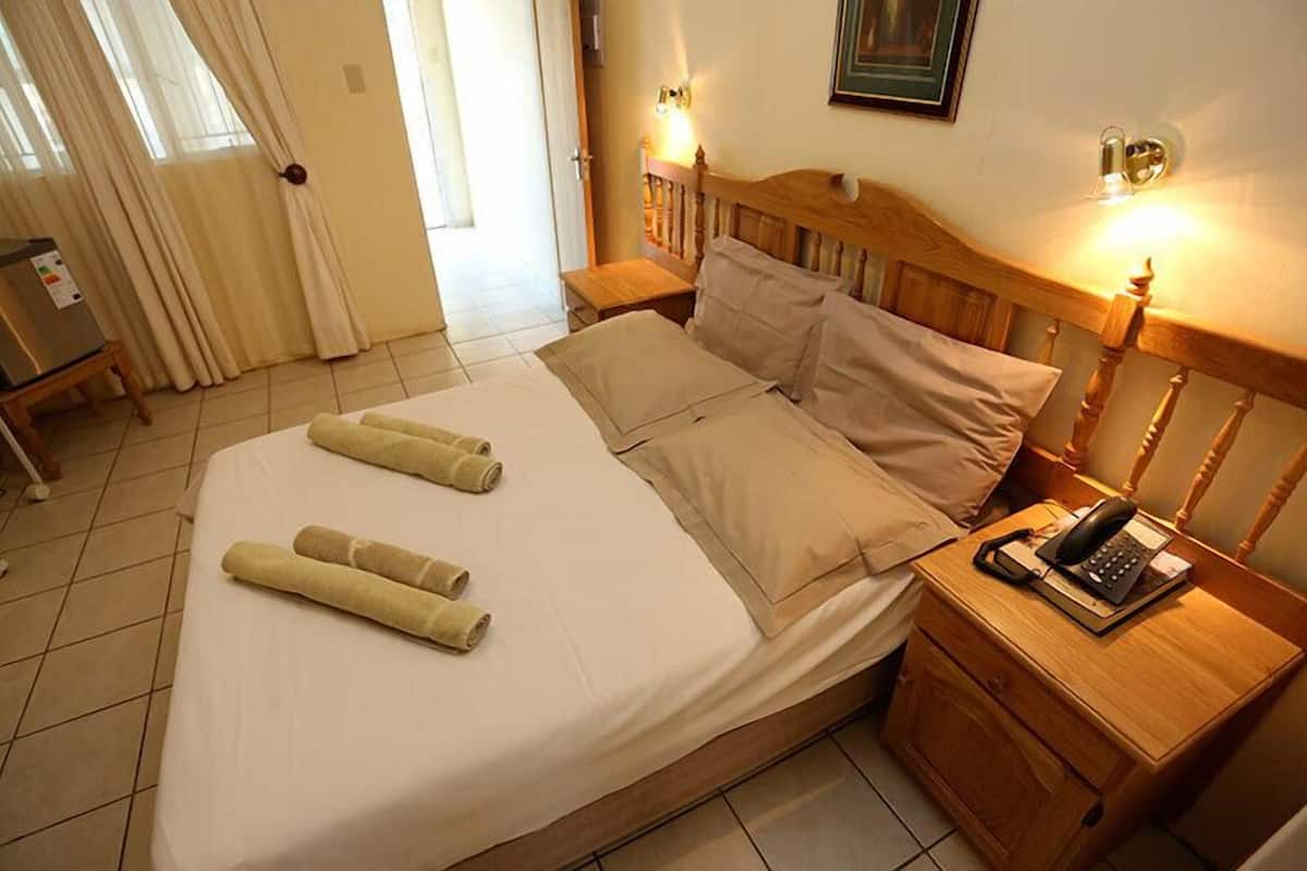 A hotel room with a bed, two bedside tables, a telephone, and a wall-mounted light fixture.
