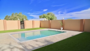 Piscina rectangular con solárium empedrado, rodeada por un bajo muro de ladrillo y un césped verde.