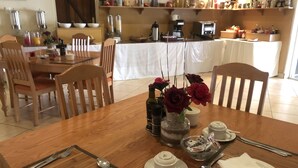 Un comedor con una mesa de madera dispuesta para cuatro personas, incluyendo platos, cubiertos y un jarrón con flores.