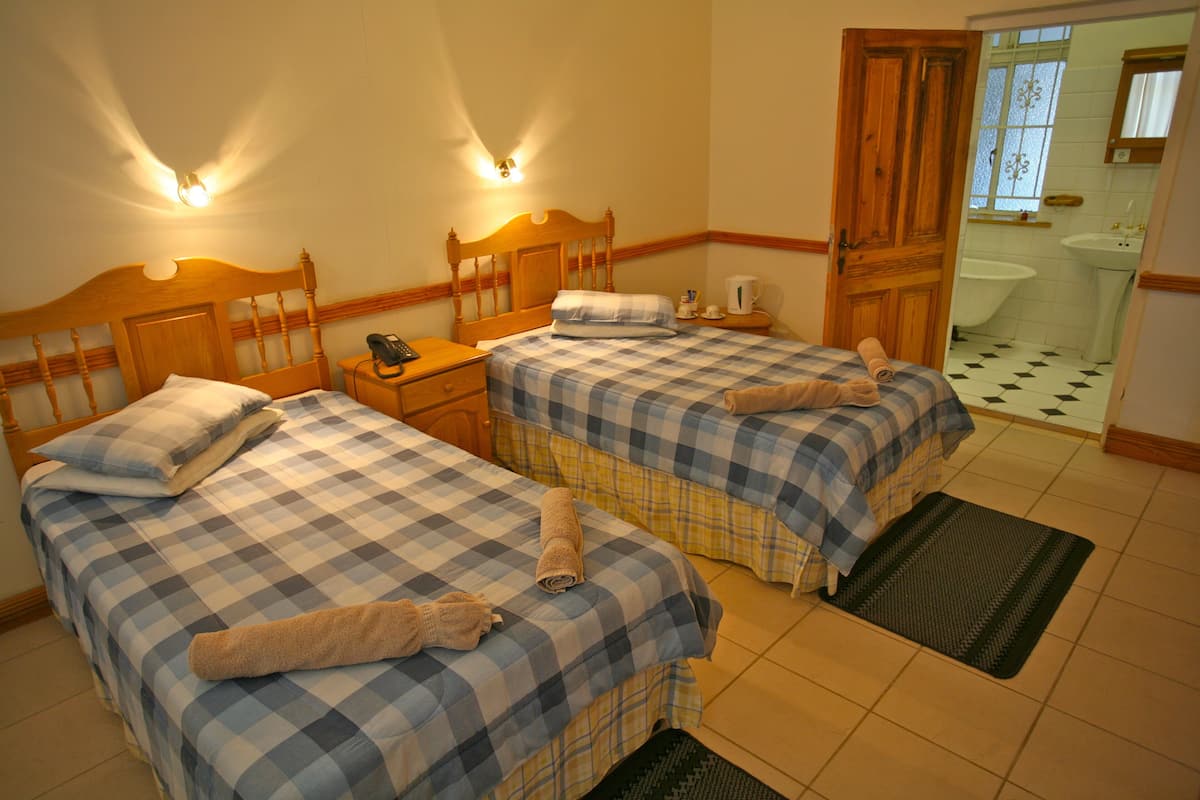 A bedroom with two beds, a nightstand, a wooden door, and a bathroom visible through an open door.
