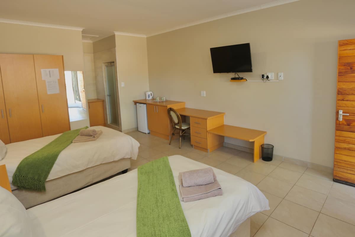 A hotel room with two beds, a desk, a chair, a television, and a wooden door.