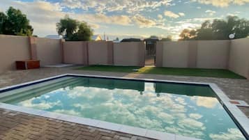 A rectangular swimming pool with a clear sky and clouds in the background.