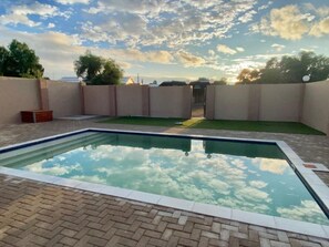 A rectangular swimming pool with a clear sky and clouds in the background. - Schuetzenhaus Guesthouse (Keetmanshoop)
