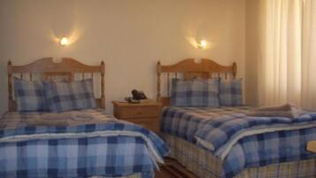 Un dormitorio con dos camas, cada una con cabecero de madera y ropa de cama de cuadros azules. Hay mesitas de noche con lámparas y un aparador con un teléfono.