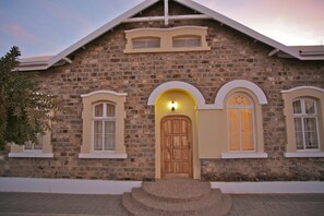 A stone building with a wooden door, two windows with white frames, and a small porch with steps.