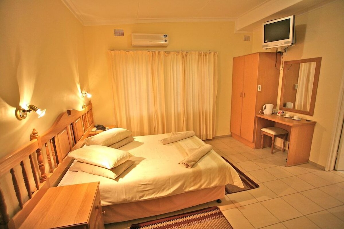 A hotel room with a bed, bedside table, lamp, TV, wardrobe, and a bathroom area.