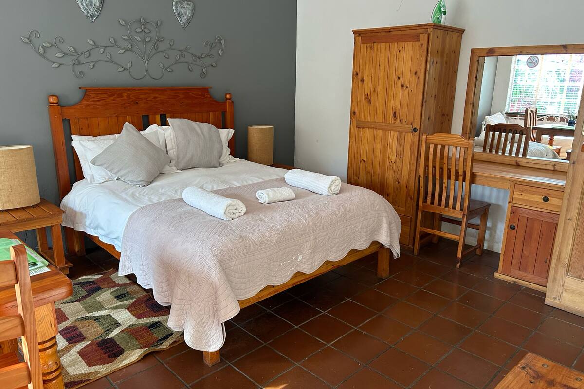 Una cama bien hecha con cabecera de madera, un armario de madera, un escritorio con silla y una alfombra estampada.