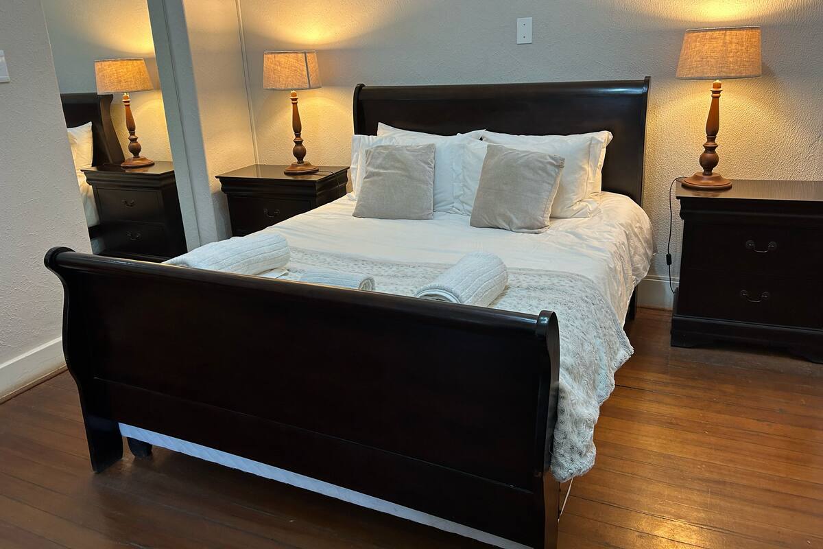 Una cama bien hecha con sábanas blancas, dos mesitas de noche con lámparas y suelo de madera.