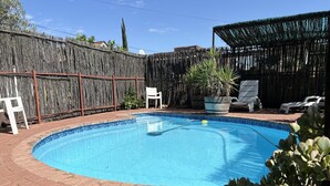 A backyard with a swimming pool, a wooden fence, and a covered seating area.