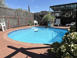 Um quintal com piscina, cerca de madeira e área de estar coberta.