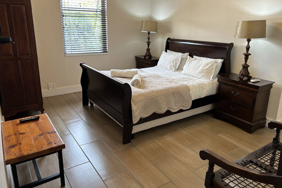 Un dormitorio con cama de madera, mesitas de noche, una silla de madera y una ventana con persianas.