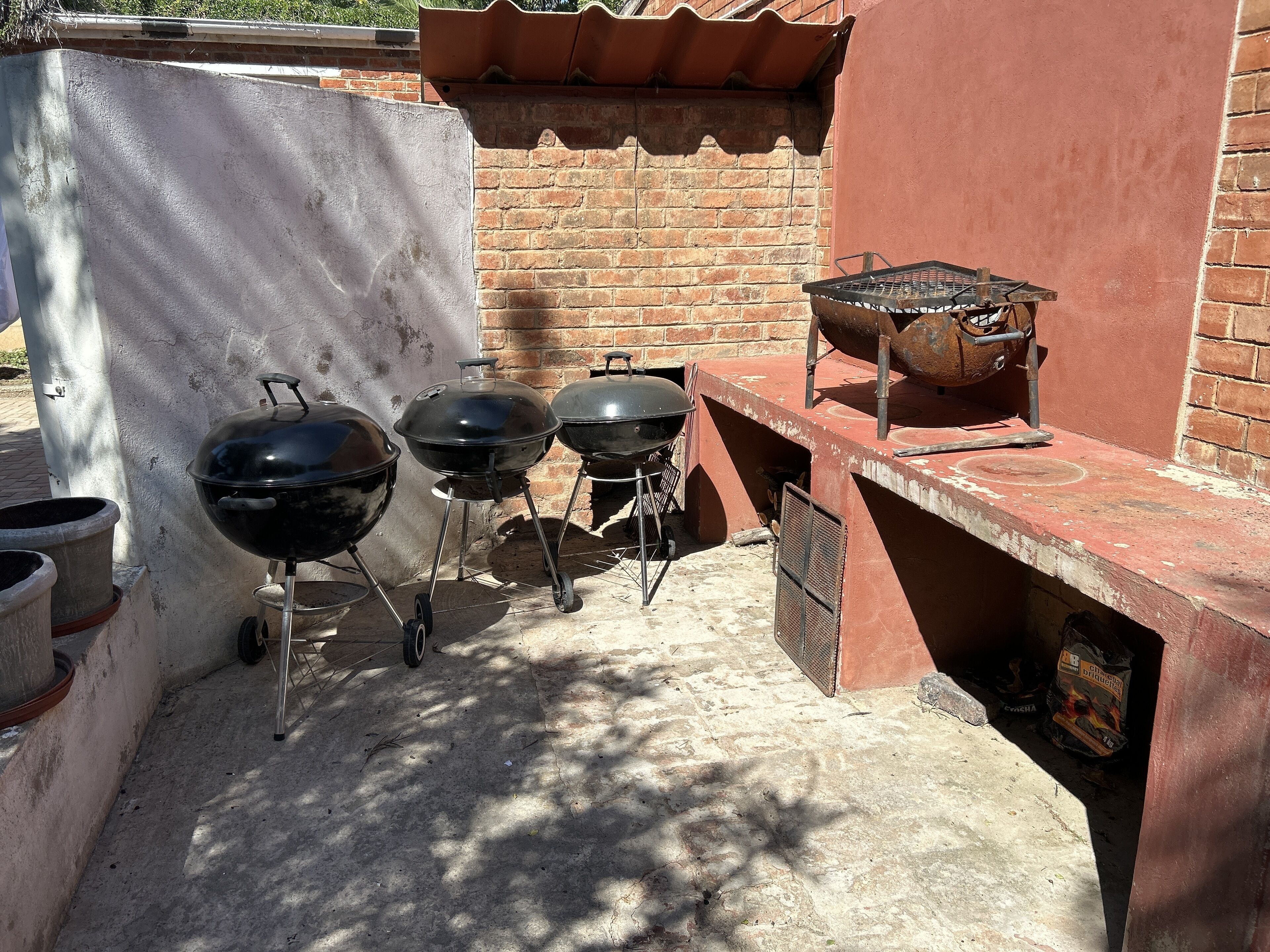 Area barbecue esterna con tre griglie, un muro in mattoni e un pavimento in cemento.