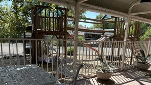 A covered outdoor area with a wooden deck, white metal chairs, and tables.