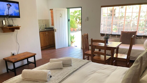 A hotel room with a bed, a wooden table, a chair, a TV, and a view of the outside.