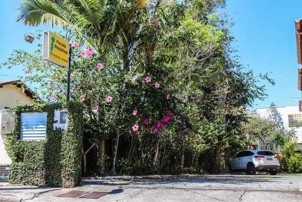 A street scene with a parked car, a building with a sign, and lush greenery. - Pousada Arquipelago (Florianópolis)