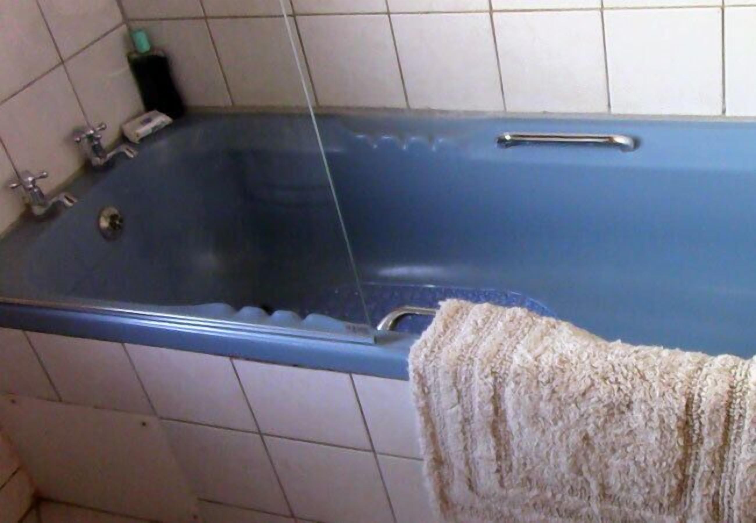 A bathroom with a blue bathtub, a towel hanging on the side, and a soap dispenser on the wall.