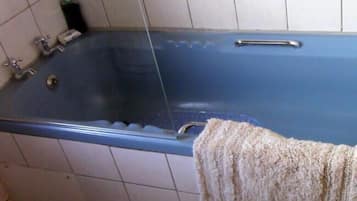 A bathroom with a blue bathtub, a towel hanging on the side, and a soap dispenser on the wall.