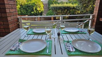 A table set for two with white plates, green placemats, and wine glasses, overlooking a landscaped garden and hills.