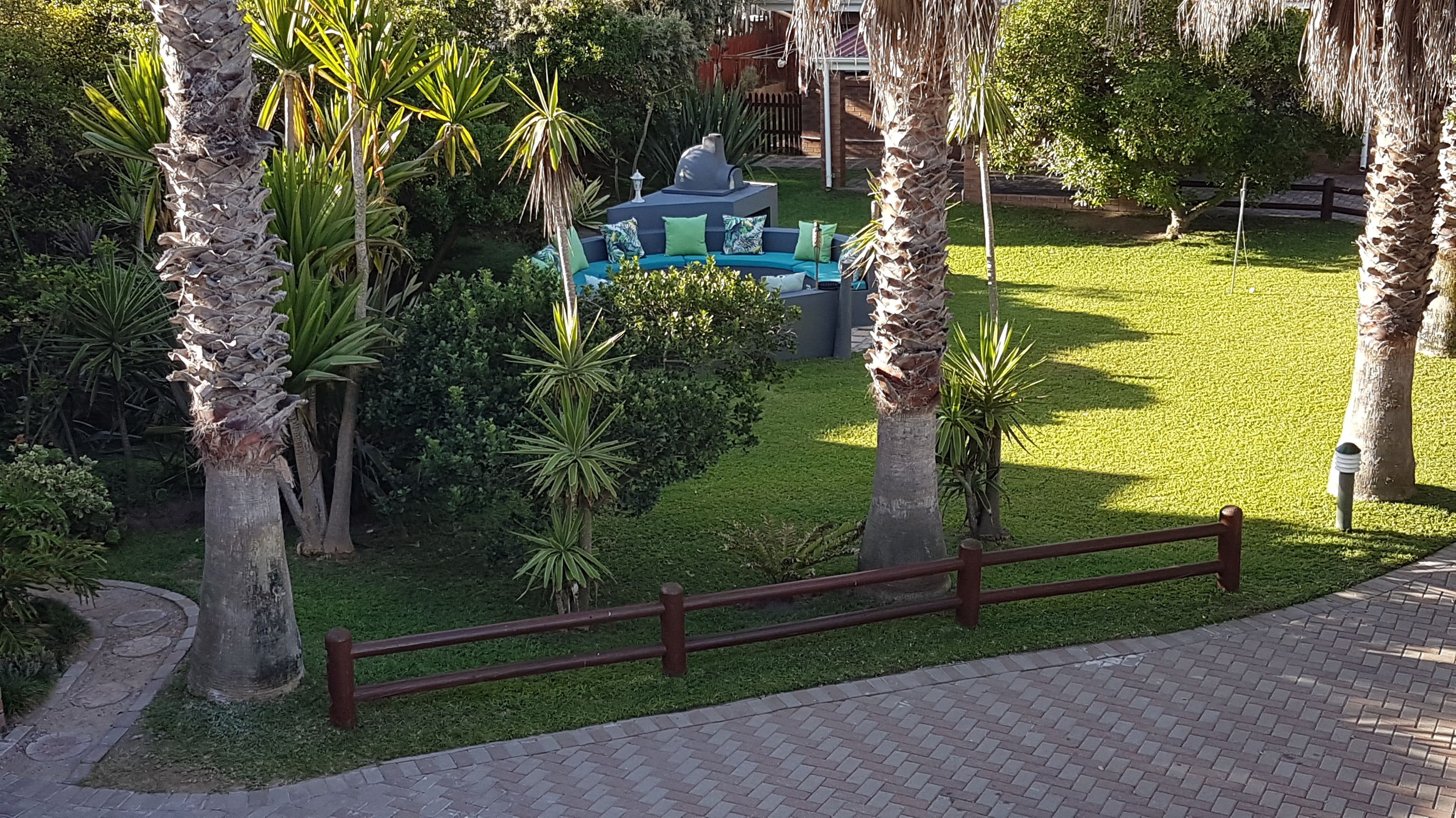 Zona de jardí amb espai per seure, palmeres i un camí.