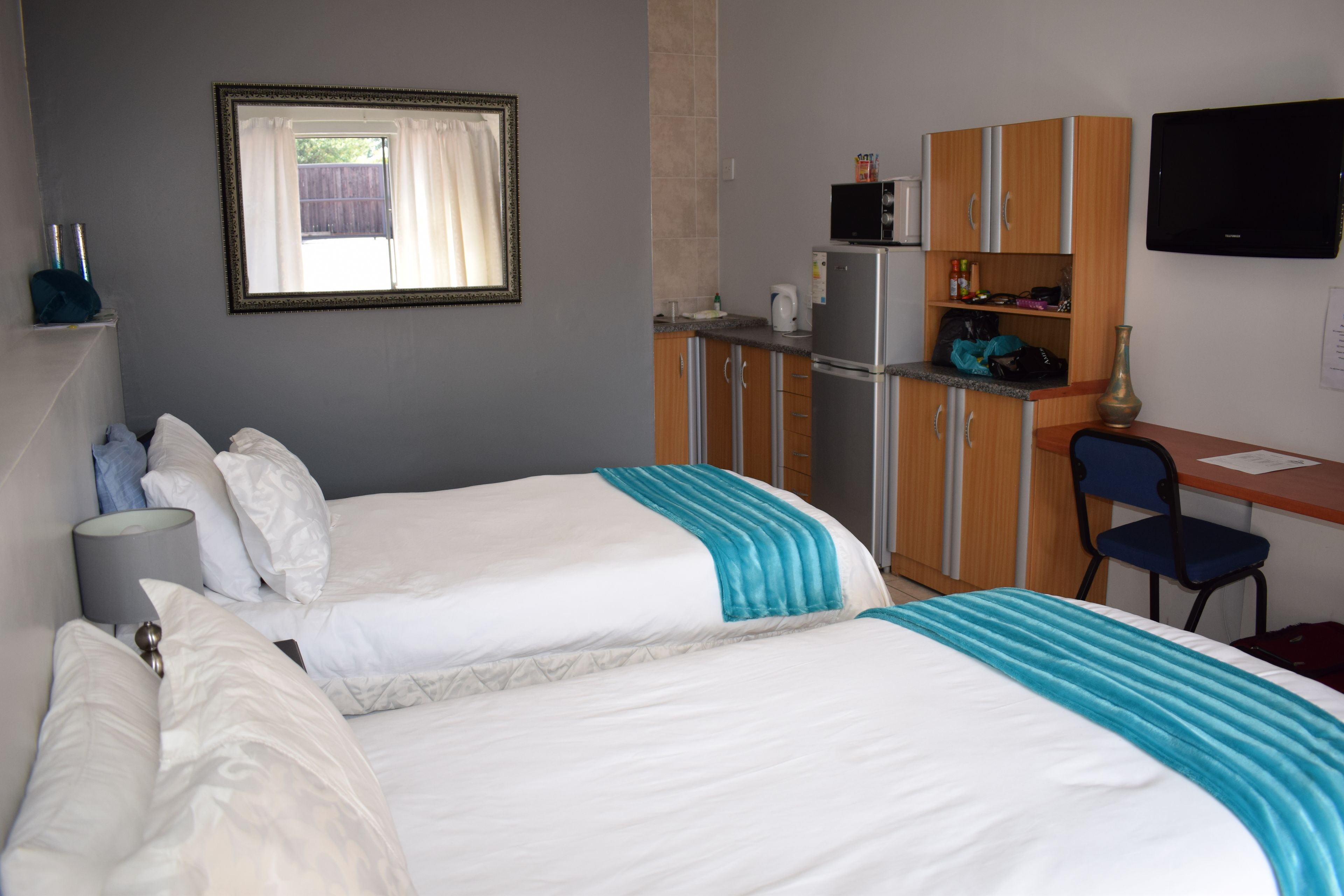 A hotel room with two beds, a desk, a chair, a TV, and a kitchenette.