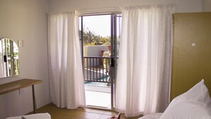 Habitación de hotel con cama, una mesita, un espejo y un ventanal corredero que da a un balcón.