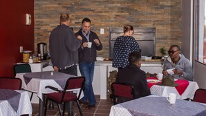Un comedor informal con mesas y sillas, una pared de ladrillo y una cocina moderna al fondo.