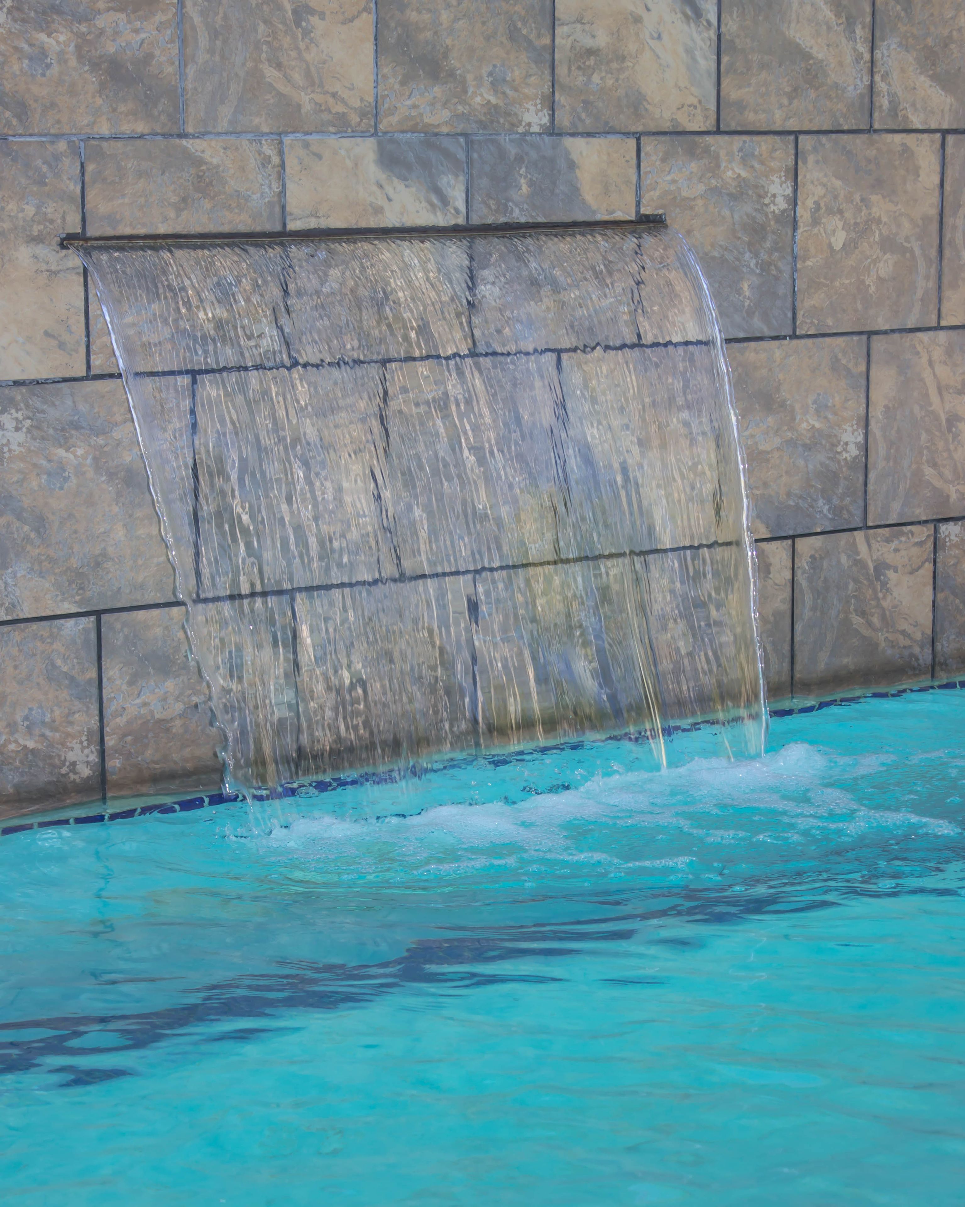 A pool with a waterfall feature against a stone wall.