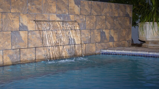 Una piscina con caída de agua, rodeada de muros de piedra y un borde de baldosas.