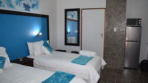 Habitación de hotel con dos camas, un refrigerador, una pared de piedra y un espejo.