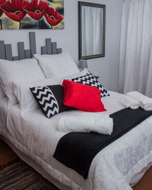 Un lit bien fait, avec une literie blanche, des coussins noirs et rouges, et un plaid noir.