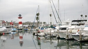 Ein Yachthafen mit mehreren vertäuten Booten, einem Leuchtturm und einem Gebäude im Hintergrund, das von Palmen gesäumt wird.