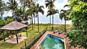 A pool area with lounge chairs and a thatched gazebo, surrounded by palm trees and a view of the ocean. - Absolute BeachFront Bliss @ Newell Beach (Newell)