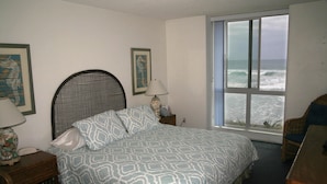 Une chambre à coucher comprenant un lit, une table de chevet, une lampe, une chaise et une fenêtre donnant sur l’océan.