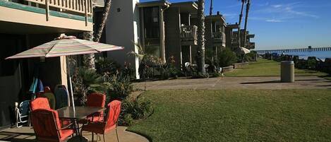 Un patio con mesa y sillas, un paraguas a rayas y vista al océano.