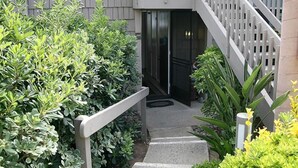 A staircase leading to a building entrance, surrounded by greenery and a white railing. - Beachfront Bungalow (Oceanside)