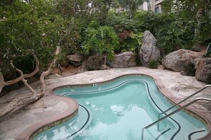 A swimming pool with a curved design, surrounded by rocks and lush greenery. - Seascape Stay (Oceanside)