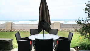 A round table with four chairs and a single umbrella, overlooking a beach with waves. - Sunset Getaway (Oceanside)