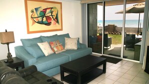 A living room with a blue sofa, a black coffee table, and a large window with a view of the ocean. - Sunset Getaway (Oceanside)