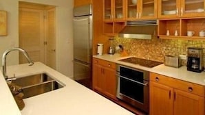 A kitchen with wooden cabinets, a stainless steel refrigerator, a sink, and a coffee maker. - Turtle Glass 309 (Port St. Joe)
