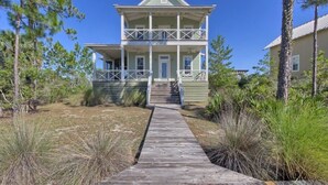 A two-story wooden house with a balcony, surrounded by pine trees and a wooden walkway leading to the entrance.