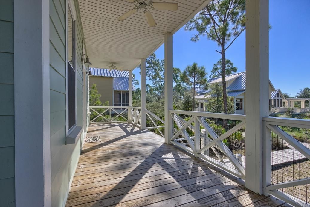 A wooden deck with a white railing, a ceiling fan, and a view of neighboring houses.