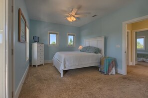 A bedroom with a bed, a ceiling fan, a dresser, and a small table with a lamp. - Holliday House (Port St. Joe)