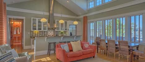 A spacious living area with a large sofa, a dining table with chairs, and a kitchen in the background.