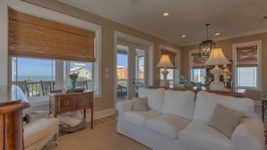 A living room with a white sofa, a wooden side table, and a lamp. There is a view of the ocean through large windows. - Cape Cottage (Port St. Joe)