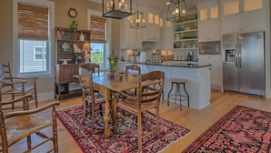 A modern kitchen with white cabinets, a stainless steel refrigerator, and a dining area with wooden chairs and a patterned rug. - Cape Cottage (Port St. Joe)