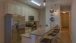 A modern kitchen with stainless steel appliances, a granite countertop, and bar stools. - Sunset Palms (Port St. Joe)