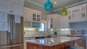 A modern kitchen with white cabinets, a stainless steel refrigerator, a central island with stools, and pendant lighting. - Sea Section (Port St. Joe)