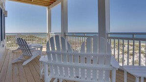A covered outdoor deck with white Adirondack chairs and a view of the beach. - Sea Section (Port St. Joe)
