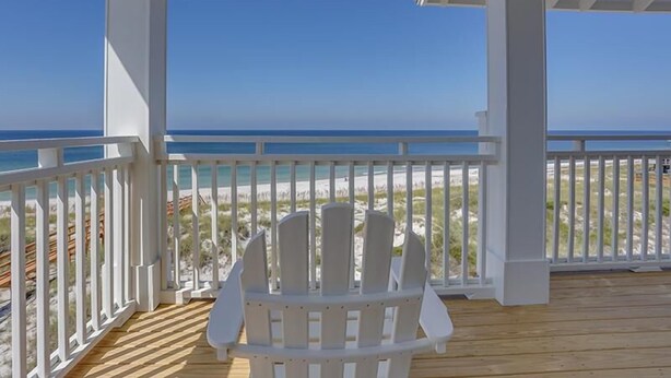 A covered outdoor area with a white Adirondack chair facing a beach. - Sea Section (Port St. Joe)